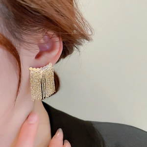 Detail view of elegant golden geometric tassel earrings on a model with metallic finish