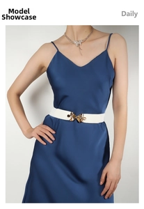 Detail of a white elastic waist belt with a gold bow buckle worn on a silk dress