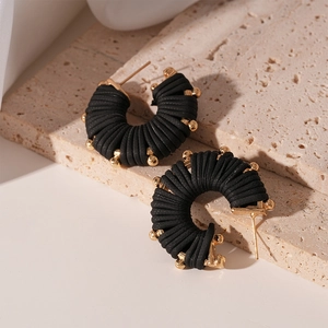 Detail of C-shaped striped faux leather earrings with gold beads on stone background