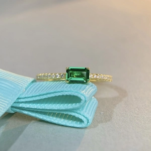 Macro shot of an emerald-cut green gemstone ring with pavé diamonds on a blue ribbon