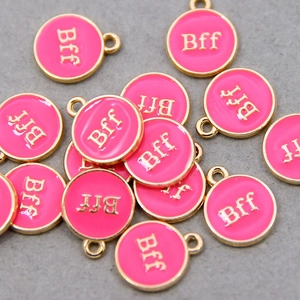 Macro shot of rose pink round oil drip charms with gold edges and Bff engraving for DIY
