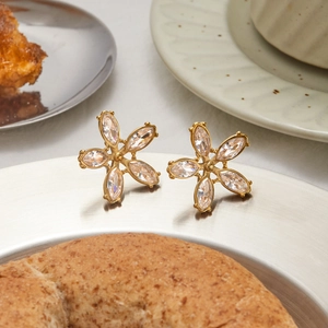 Détail de boucles d'oreilles fleurs en or avec oxydes de zirconium sur plateau argent