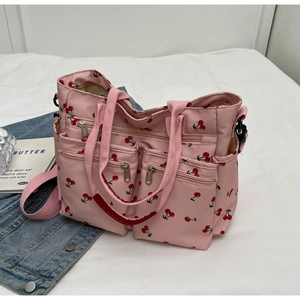 Detail of pink cherry print tote bag with multiple zippers on white bedding background