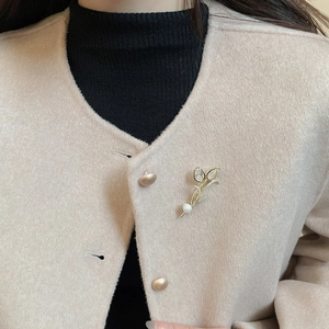 Detail of 14K gold plated tulip brooch with cubic zirconia and pearl on wool coat