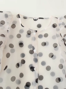 Detail of polka dot organza shirt showing sheer fabric texture and ruffle sleeve trim