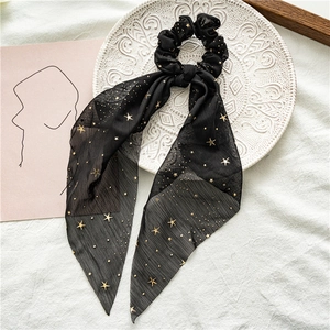 Detail of black chiffon scrunchie with gold stars and long ribbon on a white plate