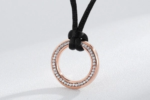 Macro detail of a rose gold circular pendant ring with fine pavé crystals on a black cord