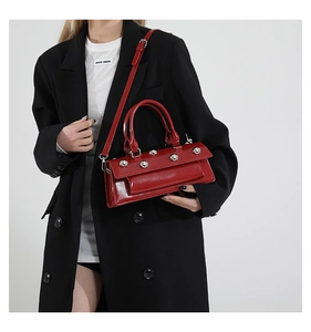 Detail of red glossy baguette bag with silver spherical rivets and adjustable shoulder strap