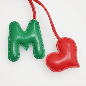 Detail of leather letter M and heart charm with hand-stitched seams for handbag