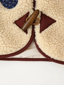 Close-up of beige faux shearling vest with brown piping and a wooden toggle button detail