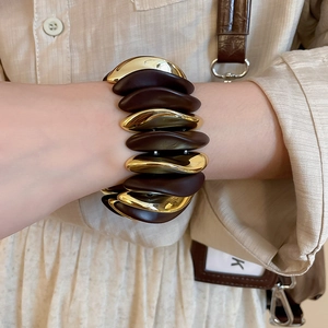 Macro shot of a layered wide cuff bracelet in gold and brown tones with a modern wavy design