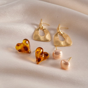 Detailed shot of mixed earrings set with resin heart and gold studs on beige silk