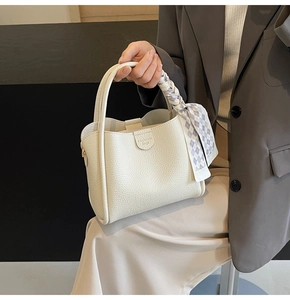 Close-up of beige lychee pattern bucket bag with woven handle and blue checkered scarf