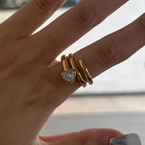 Detailed close-up of a spiral gold ring with a heart-shaped zircon on a finger