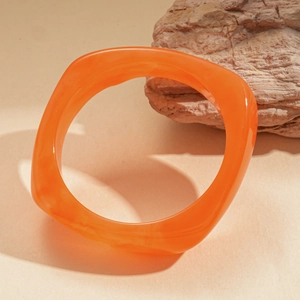 Close-up of bright orange resin bangle with swirled texture on a neutral stone