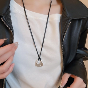 Close-up of a silver handbag-shaped pendant on a black cord necklace worn on a model