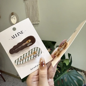 Close-up of wavy hair clips in brown and green-white stripes on a display card