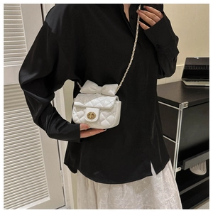Detailed view of mini white quilted crossbody bag with bow decoration and golden twist lock