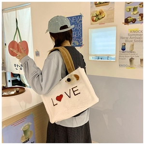 Detail of white plush tote bag with LOVE embroidery and cute dog charm in a cafe