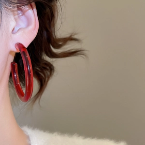 Detail of dark red resin C-shape hoop earring worn on model ear for autumn style
