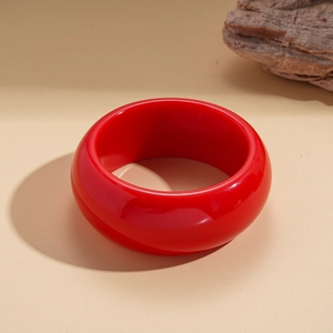 Detail shot of a wide red acrylic bangle with glossy finish and geometric round design