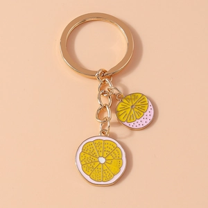 Close-up of golden keychain with two realistic yellow lemon slice pendants on beige background