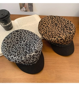 Top view of stylish leopard print baker boy hats in gray and brown on a wooden desk