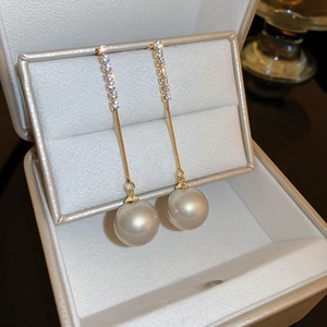Détail de boucles d'oreilles pendantes dorées avec cristaux et perles blanches