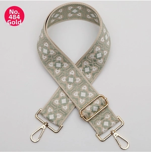 Detail of a wide woven guitar-style bag strap with green geometric patterns and gold buckles