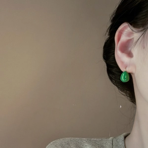 Close-up of emerald green teardrop earrings with elegant gold hooks on model
