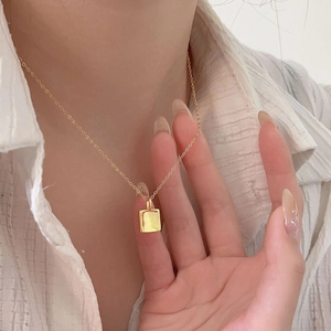 Detail of a minimalist gold square pendant necklace on a model wearing white shirt