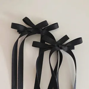 Détail de nœuds à cheveux en satin noir avec de longs rubans sur fond minimaliste