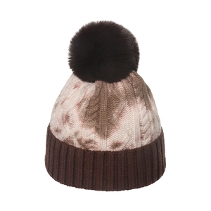 Detail of winter cable knit beanie with brown tie-dye pattern and large faux fur pompom