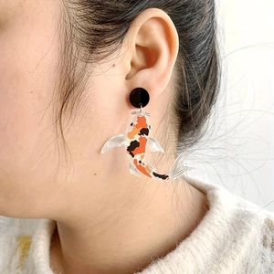 Detail of koi fish acrylic earrings worn by model, showing orange and black artistic patterns