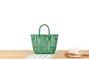 Vue détaillée d'un mini sac cabas tressé vert métallisé posé sur une table en bois