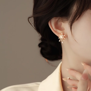 Close-up of golden snowflake stud earring with central pearl and sparkling zircon stones