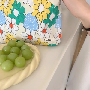 Detail of floral daisy cotton makeup bag with brand tag and metal zipper on white base