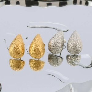 Matte gold and silver hollow teardrop earrings displayed on a reflective water surface