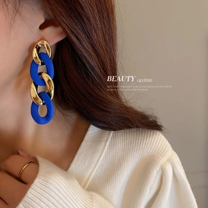 Fashionable Klein blue and gold chain drop earrings worn by a model in warm lighting