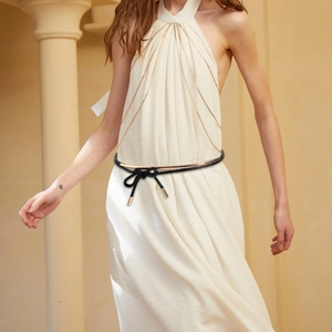 Close-up of a black woven belt with gold metal accents tied on a white dress