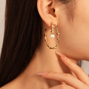 Gold bamboo hoop earrings with zircon and pearl on female model in warm studio lighting