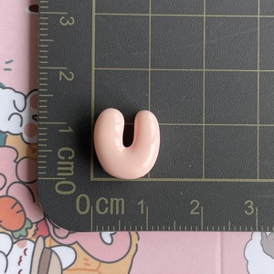Pink resin U-letter accessory measuring 1cm by 1cm on a black metric scale grid