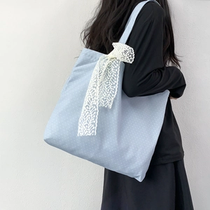 Detail view of light blue polka dot tote bag with a white lace bow on shoulder