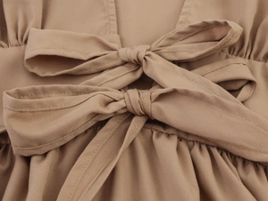 Detail of light brown dress featuring elegant double bow tie-up front and fabric texture