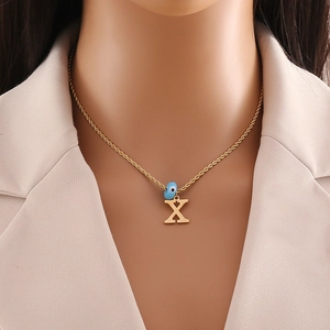 Detail view of gold rope chain with uppercase letter X and blue evil eye bead on a neck