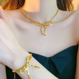 Ensemble collier et bracelet dorés avec nœud et pompons sur mannequin femme