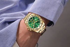 Close-up of gold stainless steel watch with green dial worn on wrist over a blue shirt