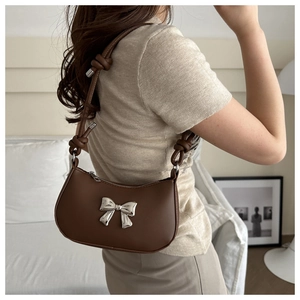Brown leather shoulder bag featuring a decorative silver metal bow and knotted strap detail