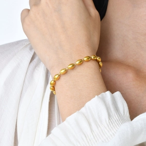 Detail view of 18K gold-plated oval bead chain bracelet on a wrist with white cuff