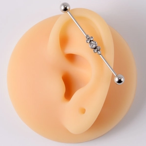 Detail of silver stainless steel industrial barbell piercing with flower crystals on ear